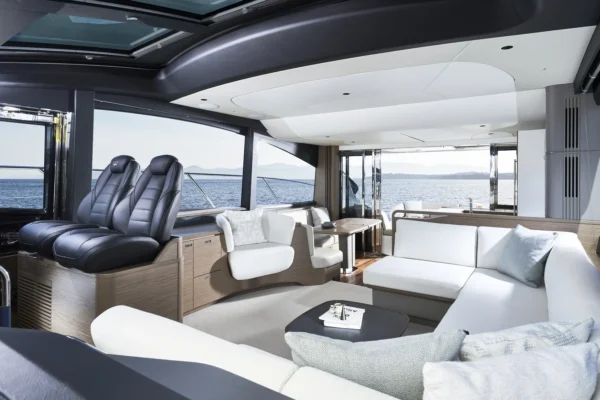 Moderner Salonbereich der Princess S65 mit nach hinten gerichteten Sitzmöglichkeiten, stilvollen schwarzen Kapitänssitzen und einem eleganten Lounge-Sofa. Die großzügigen Fenster bieten einen ungestörten Blick auf das Meer und füllen den Raum mit natürlichem Licht.