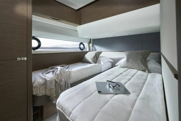 Seitliche Gästekabine der Princess S65 mit zwei Einzelbetten, schlichtem Design und einem Fenster mit Blick aufs Meer. Ein Tablet und eine Brille liegen auf dem Bett, was eine entspannte Atmosphäre unterstreicht.